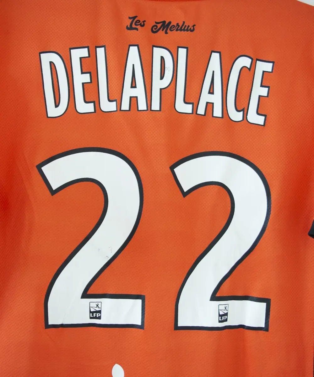 Maillot domicile de Lorient de la saison 2018-2019 de couleur orange, blanc et noir. On peut retrouver l'équipementier kappa et les sponsors jean floc'h, b&b et breizh cola. Le maillot est floqué du numéro 22 delaplace et signé par plusieurs joueurs de l'équipe