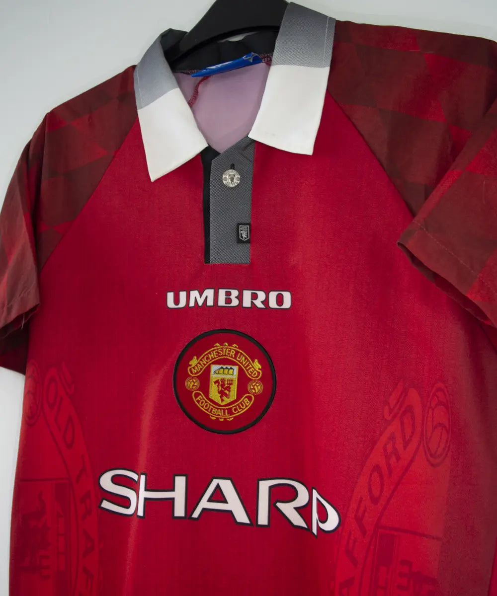 Maillot de foot vintage domicile rouge de manchester united de la saison 1996-1998. On peut retrouver l'équipementier umbro et le sponsor sharp. Le maillot est floqué du numéro 7 Cantona. Il s'agit d'un maillot authentique