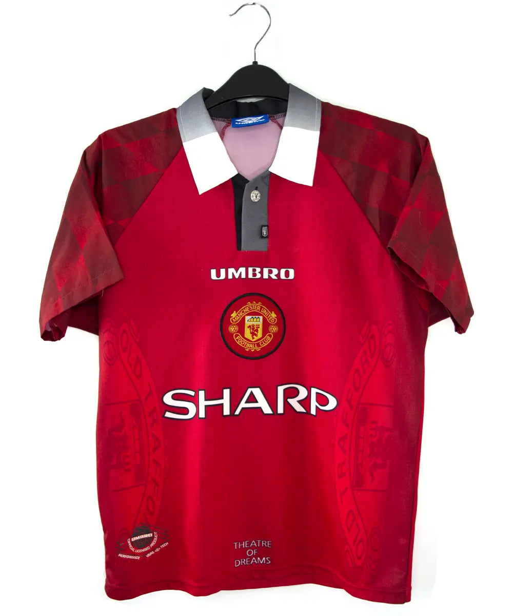 Maillot de foot vintage domicile rouge de manchester united de la saison 1996-1998. On peut retrouver l'équipementier umbro et le sponsor sharp. Le maillot est floqué du numéro 7 Cantona. Il s'agit d'un maillot authentique