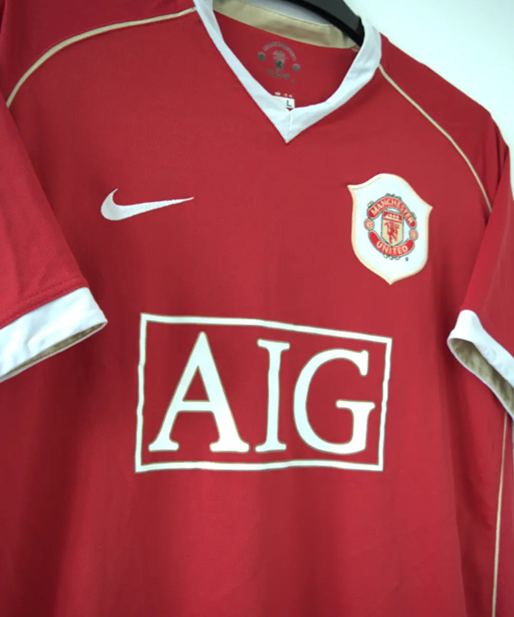 Maillot domicile rouge de manchester united de la saison 2006-2007. Le maillot est floqué du numéro 7 cristiano ronaldo. Sur cette photo on peut voir le devant du maillot avec le sponsor AIG et l'équipementier nike. Sur cette photo on peut voir le devant du maillot de côté