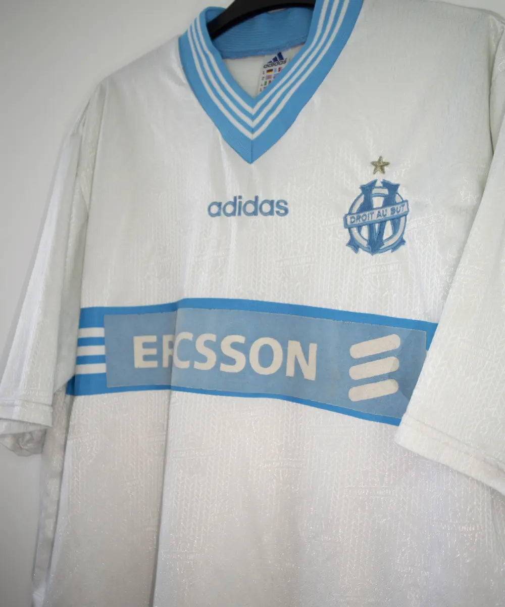 Maillot vintage domicile banc et bleu de l'OM de la saison 1997-1998. On peut retrouver l'équipementier adidas et le sponsor ericsson