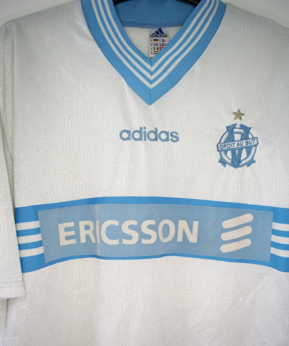 Maillot vintage domicile banc et bleu de l'OM de la saison 1997-1998. On peut retrouver l'équipementier adidas et le sponsor ericsson