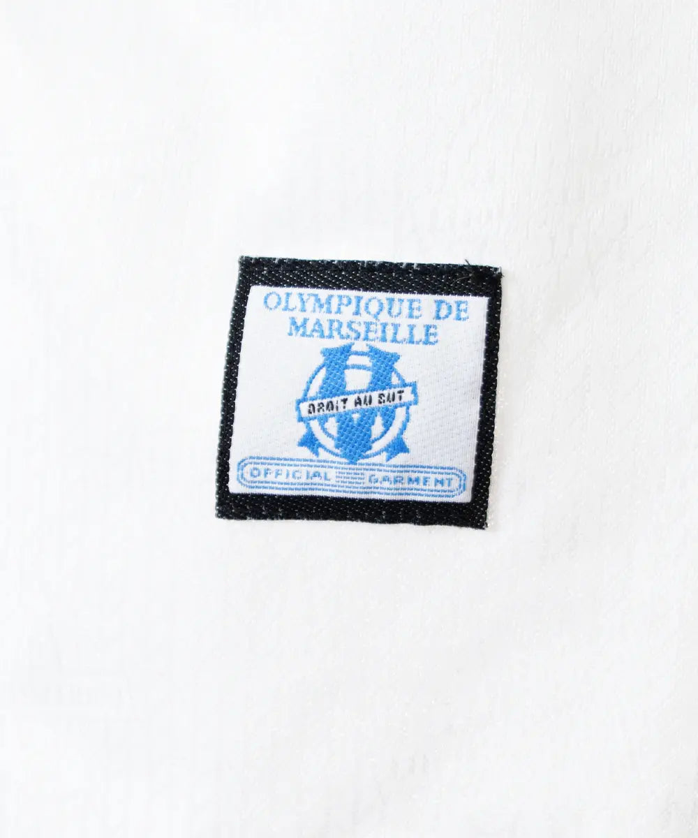Maillot domicile blanc et bleu de l'olympique de marseille de la saison 1997-1998. Le maillot est floqué du numéro 5 Laurent Blanc. Sur cette photo on peut voir le devant du maillot avec sponsor ericsson et l'équipementier adidas. Sur cette photo on peut voir le patch adidas official garment