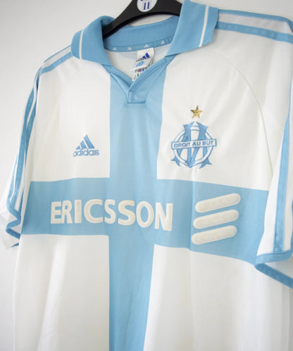 Maillot de foot vintage de l'om de la saison 2000-2001. Le maillot est de couleur blanc et bleu. On peut retrouver l'équipementier adidas et le sponsor ericsson. Ils s'agit d'un maillot authentique