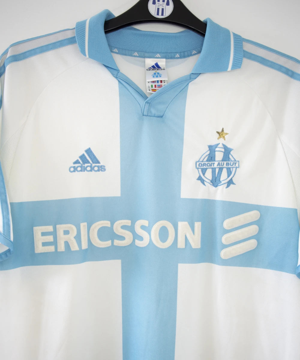 Maillot de foot vintage de l'om de la saison 2000-2001. Le maillot est de couleur blanc et bleu. On peut retrouver l'équipementier adidas et le sponsor ericsson. Ils s'agit d'un maillot authentique