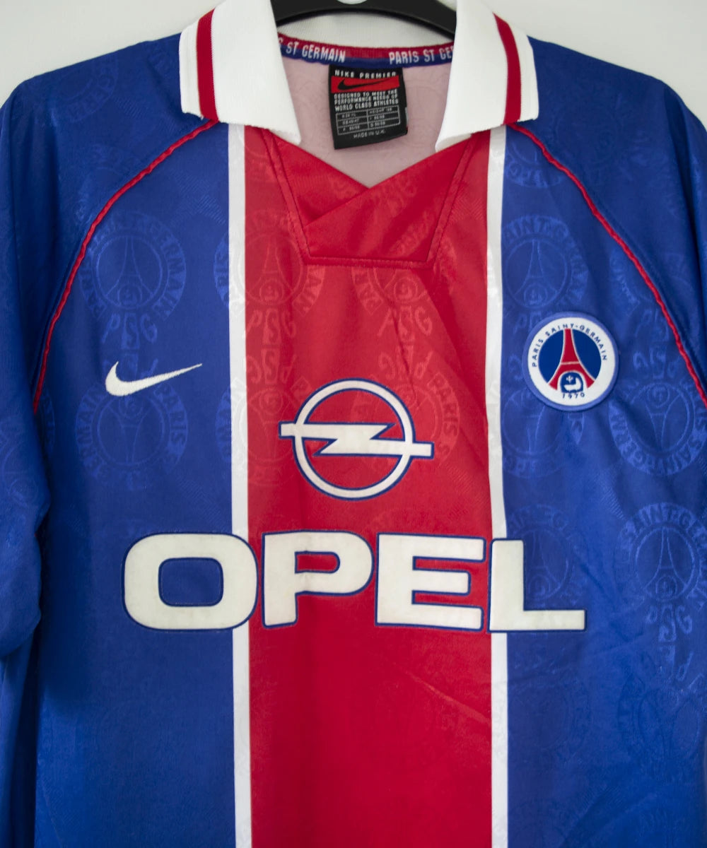 Maillot de foot vintage bleu blanc et rouge du psg de la saison 1996/1997. On peut retrouver l'équipementier nike et le sponsor opel. Il s'agit d'un maillot authentique d'époque
