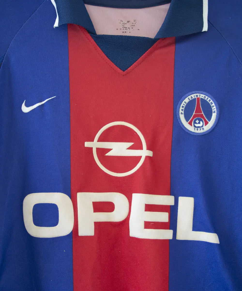 Maillot authentique domicile du PSG de la saison 2000-2001. Le maillot est de couleur bleu et rouge. On peut retrouver l'équipementier nike et le sponsor opel en feutrine. Le maillot est floqué du numéro 10 okocha. Sur cette photo on peut voir le maillot de près