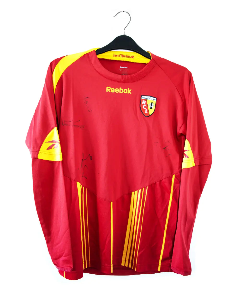 Maillot domicile rouge et jaune du rc lens de la saison 2009-2010. On peut retrouver l'équipementier reebok. Le maillot est également signé.