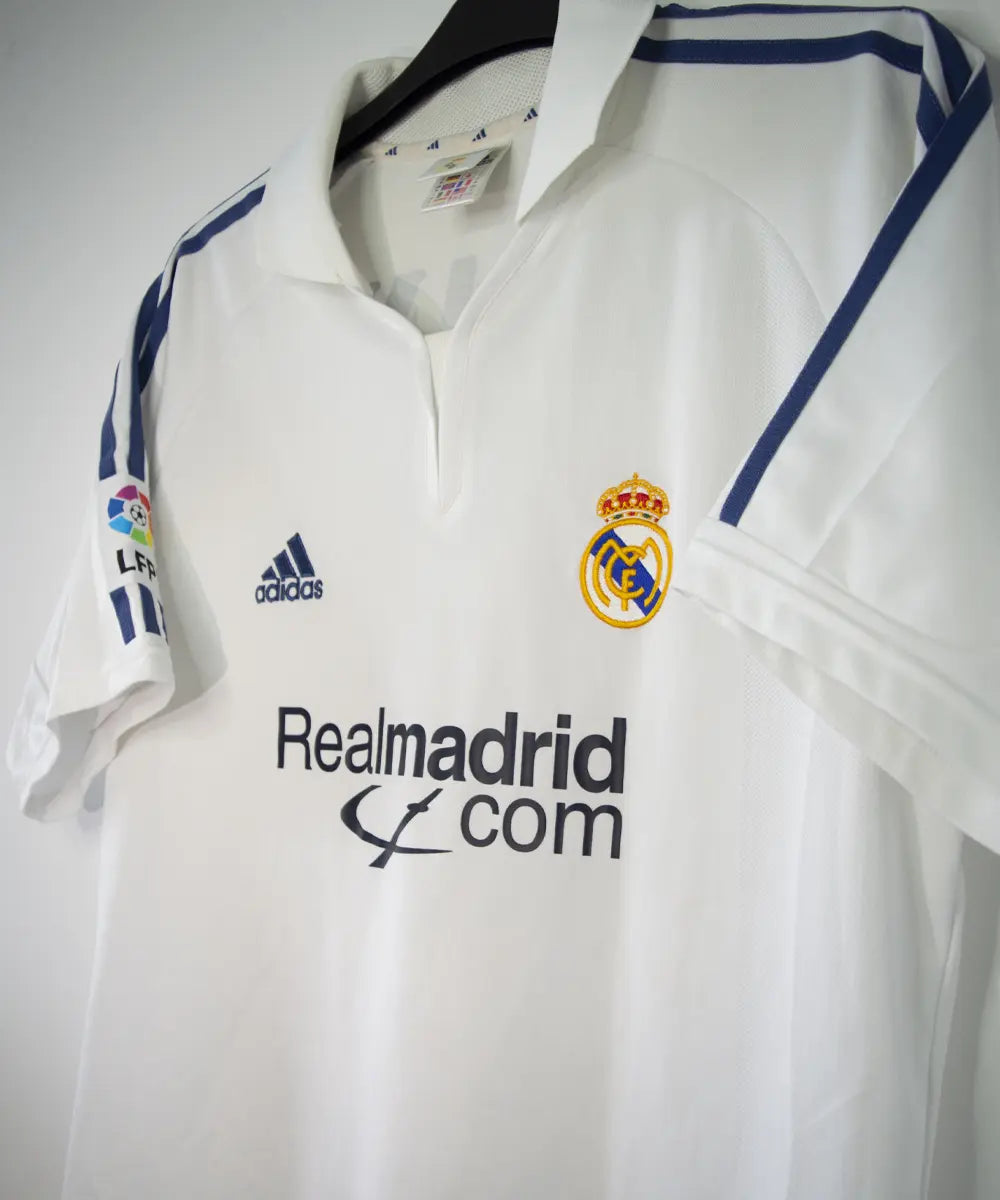 Maillot de foot vintage blanc domicile du real madrid de la saison 2001-2002. Il s'agit du maillot édité pour le centenaire. On peut retrouver l'équipementier adidas et le sponsor real madrid.com. Le maillot est floqué du numéro 5 Zidane. Le maillot comporte l'étiquette 695856 ASR001/09