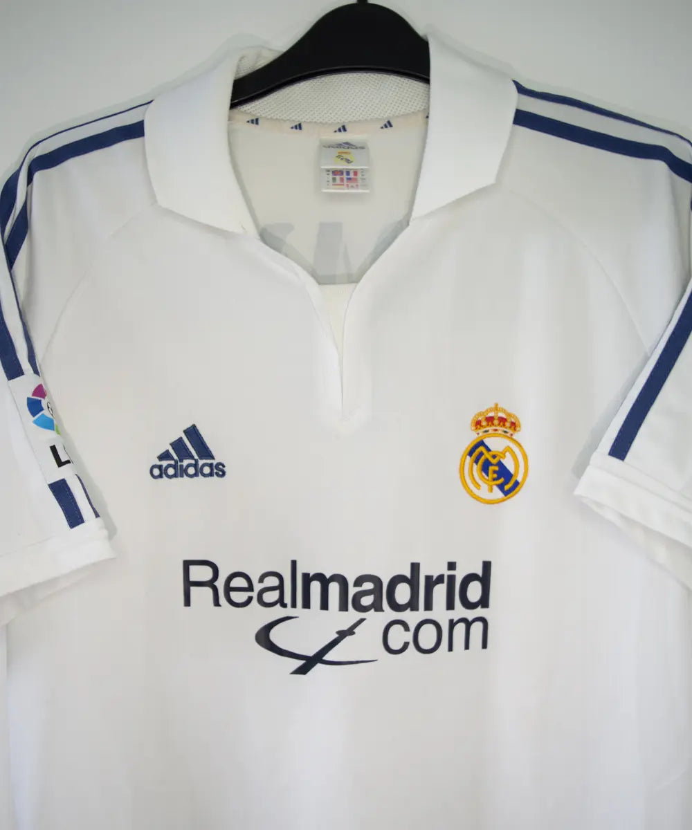 Maillot de foot vintage blanc domicile du real madrid de la saison 2001-2002. Il s'agit du maillot édité pour le centenaire. On peut retrouver l'équipementier adidas et le sponsor real madrid.com. Le maillot est floqué du numéro 5 Zidane. Le maillot comporte l'étiquette 695856 ASR001/09