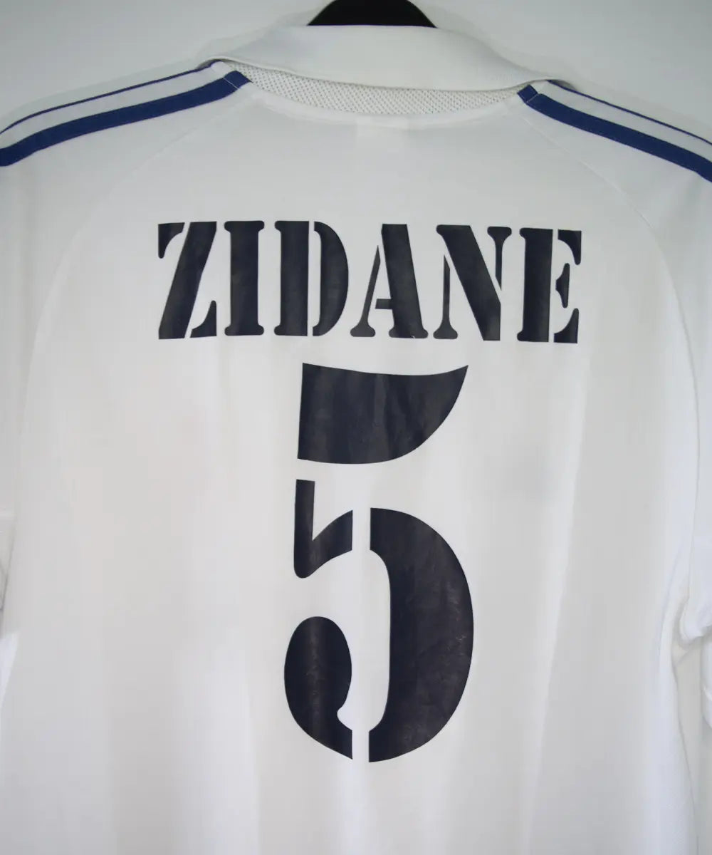 Maillot de foot vintage blanc domicile du real madrid de la saison 2001-2002. Il s'agit du maillot édité pour le centenaire. On peut retrouver l'équipementier adidas et le sponsor real madrid.com. Le maillot est floqué du numéro 5 Zidane. Le maillot comporte l'étiquette 695856 ASR001/09