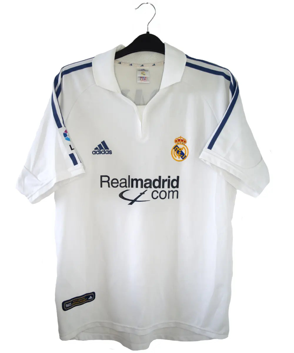 Maillot de foot vintage blanc domicile du real madrid de la saison 2001-2002. Il s'agit du maillot édité pour le centenaire. On peut retrouver l'équipementier adidas et le sponsor real madrid.com. Le maillot est floqué du numéro 5 Zidane. Le maillot comporte l'étiquette 695856 ASR001/09