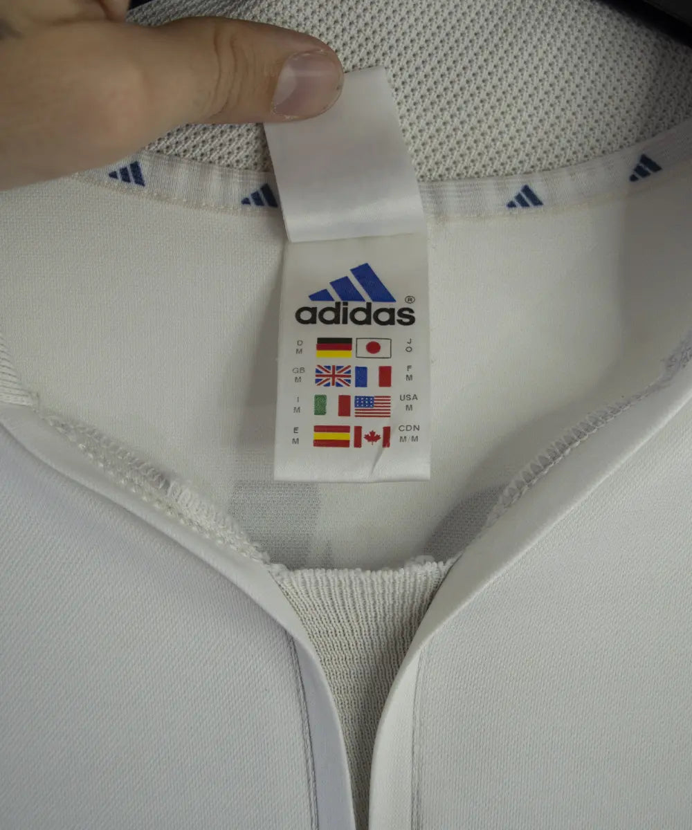 Maillot de foot vintage blanc et bleu du real madrid de la saison 2001-2002. On peut retrouver l'équipementier adidas et le sponsor real madrid.com. Le maillot est flqqué du numéro 5 Zinedine Zidane. Il s'agit d'un maillot authentique.