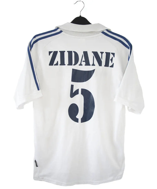 Maillot de foot vintage blanc et bleu du real madrid de la saison 2001-2002. On peut retrouver l'équipementier adidas et le sponsor real madrid.com. Le maillot est flqqué du numéro 5 Zinedine Zidane. Il s'agit d'un maillot authentique.