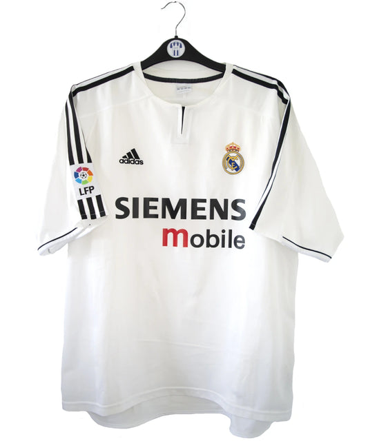 Maillot de foot vintage domicile blanc et noir du real madrid de la saison 2003/2004. On peut retrouver l'équipementier adidas et le sponsor siemens mobile. On peut retrouver l'étiquette d'authenticité du maillot comportant les numéros 021804