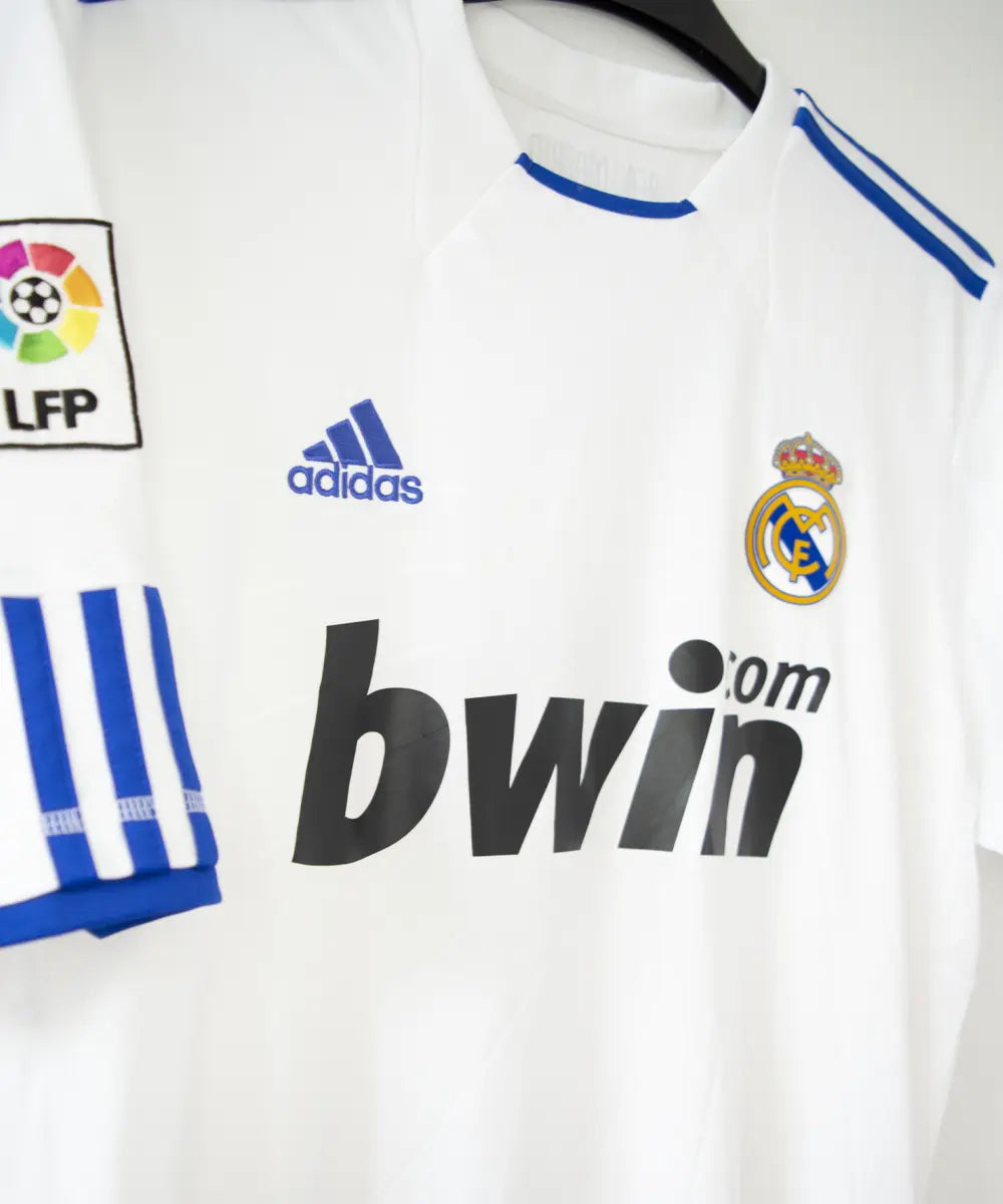 Maillot domicile du real madrid de la saison 2010-2011. Le maillot est floqué du numéro 7 cristiano ronaldo. Sur ce maillot on peut retrouver le sponsor bwin et l'équipementier adidas ainsi que le patch de la LFP. Sur cette photo on peut voir le devant du maillot de côté