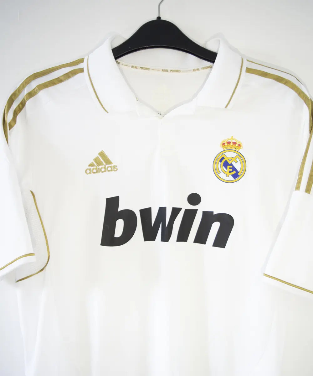 Maillot domicile du real madrid de couleur blanc et or de la saison 2011-2012. On peut retrouver l'équipementier adidas et le sponsor bwin. Le maillot est floqué du numéro 7 Cristiano Ronaldo. L'étiquette du maillot comporte les numéro V13659