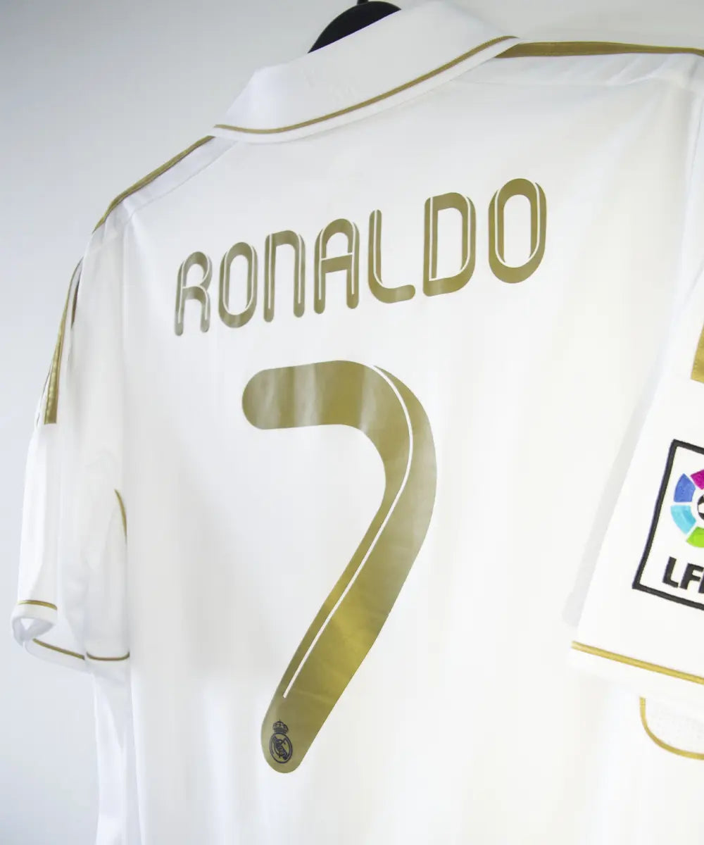 Maillot domicile du real madrid de couleur blanc et or de la saison 2011-2012. On peut retrouver l'équipementier adidas et le sponsor bwin. Le maillot est floqué du numéro 7 Cristiano Ronaldo. L'étiquette du maillot comporte les numéro V13659