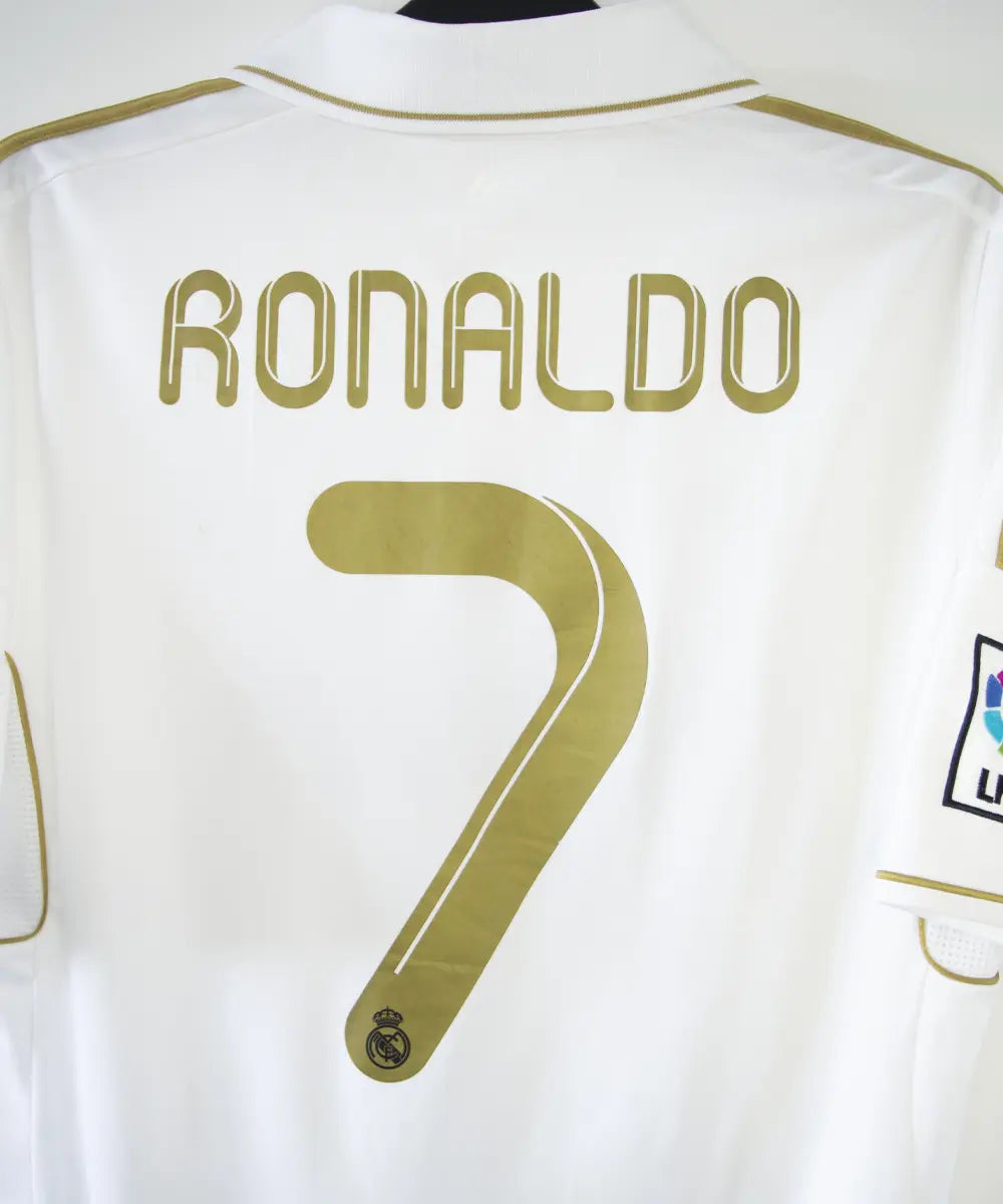 Maillot domicile du real madrid de couleur blanc et or de la saison 2011-2012. On peut retrouver l'équipementier adidas et le sponsor bwin. Le maillot est floqué du numéro 7 Cristiano Ronaldo. L'étiquette du maillot comporte les numéro V13659