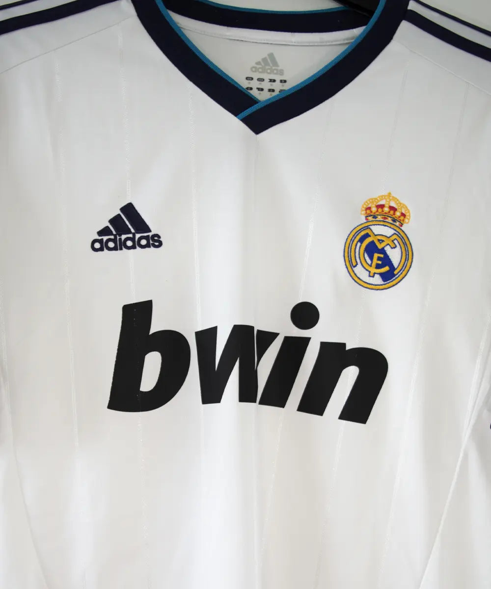 Maillot blanc et bleu du real madrid de la saison 2012-2013. On peut retrouver sur le maillot le sponsor bwin et l'équipementier adidas. Le maillot porte aussi le patch des 110 ans du real et le patch de la LFP. Sur cette photo on peut voir le devant du maillot de près