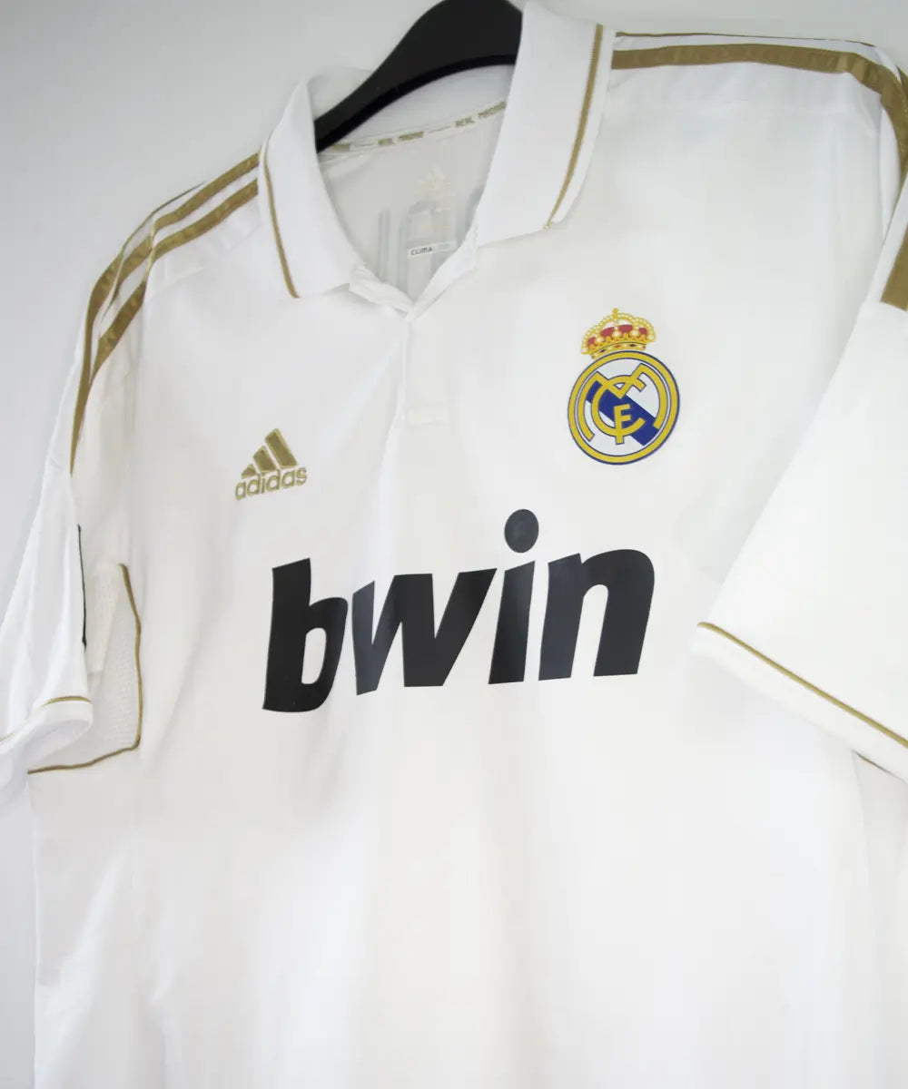 Maillot domicile du real madrid de couleur blanc et or de la saison 2011-2012. On peut retrouver l'équipementier adidas et le sponsor bwin. Le maillot est floqué du numéro 7 Cristiano Ronaldo. L'étiquette du maillot comporte les numéro V13659