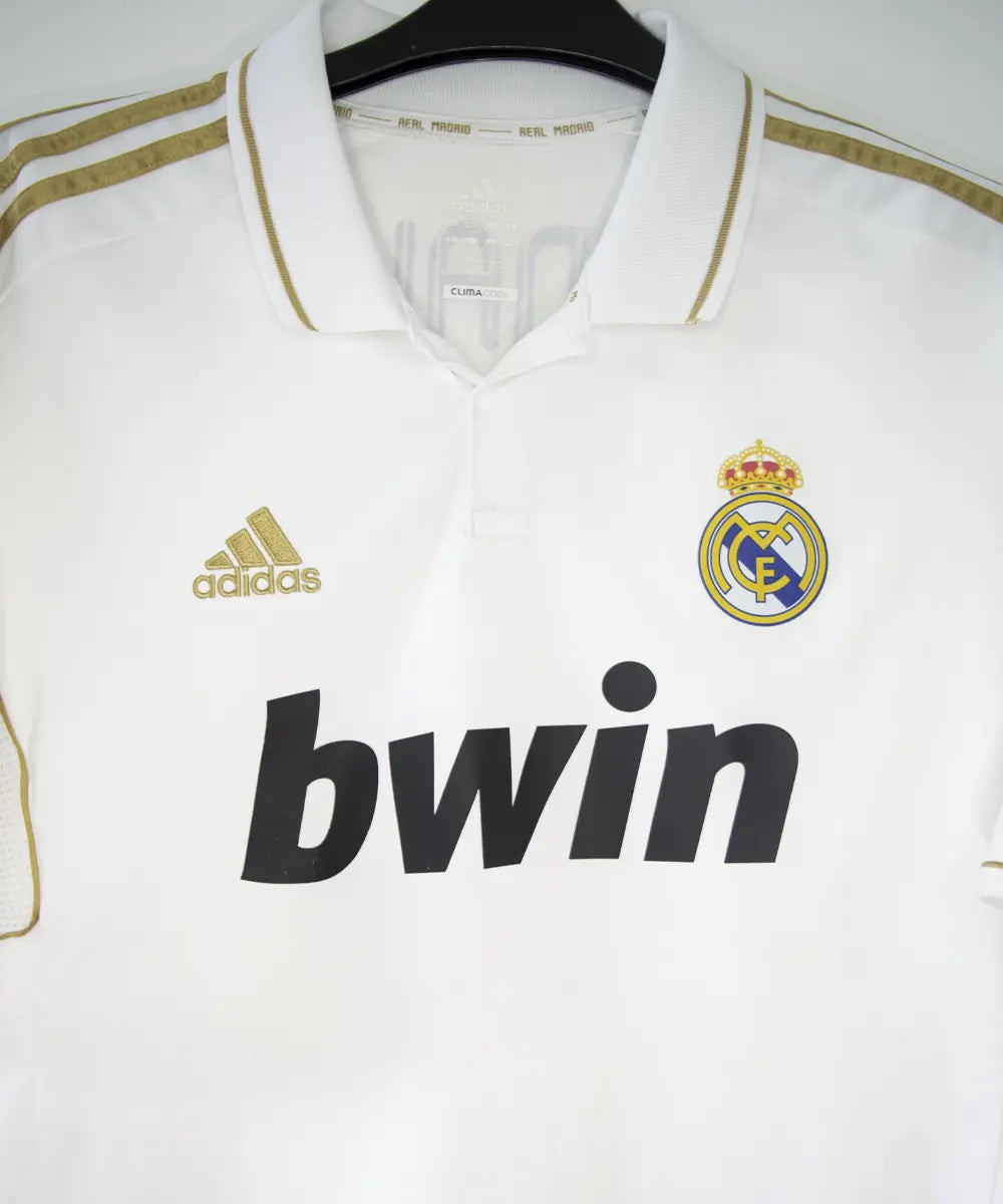 Maillot domicile du real madrid de couleur blanc et or de la saison 2011-2012. On peut retrouver l'équipementier adidas et le sponsor bwin. Le maillot est floqué du numéro 7 Cristiano Ronaldo. L'étiquette du maillot comporte les numéro V13659