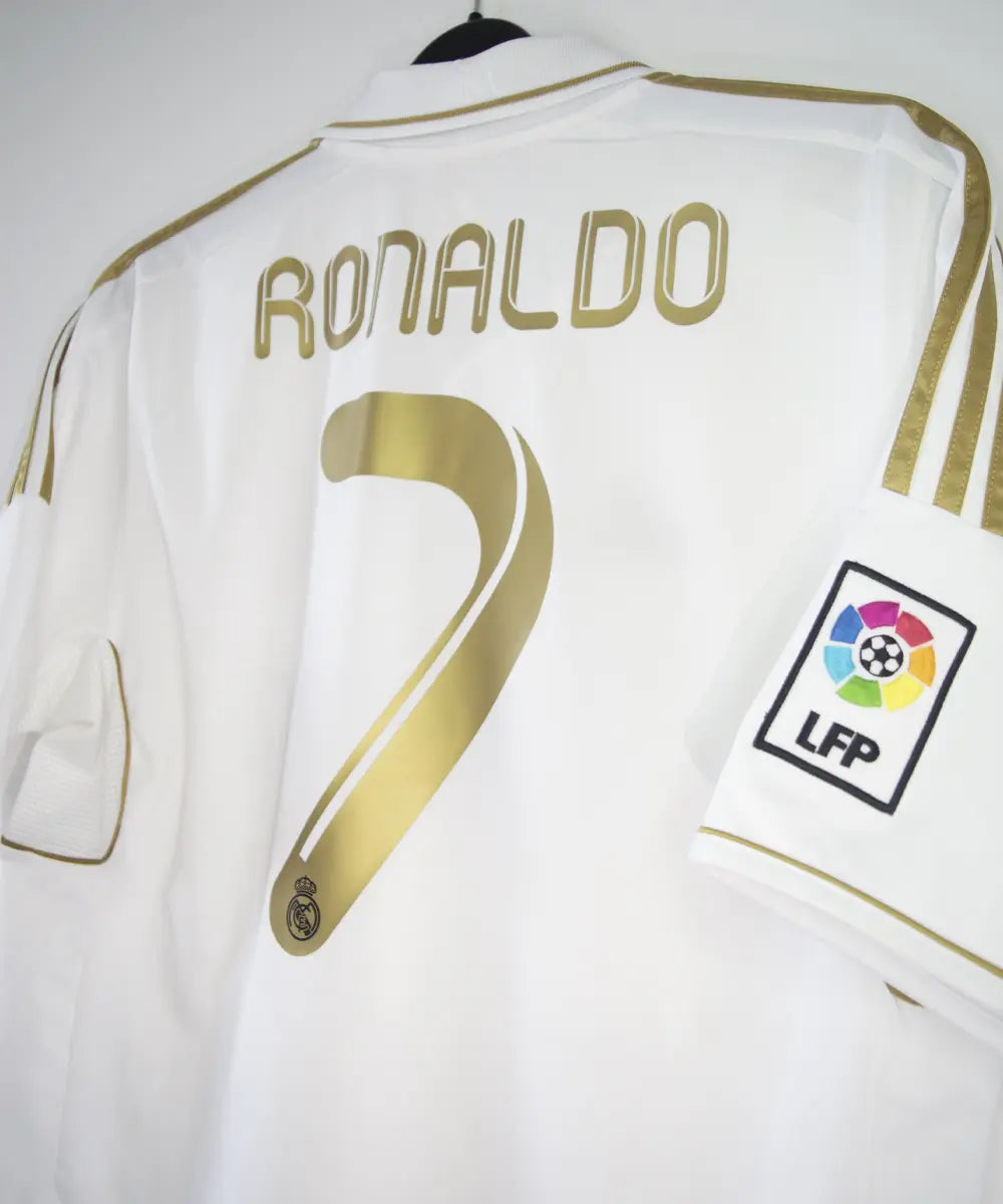 Maillot domicile du real madrid de couleur blanc et or de la saison 2011-2012. On peut retrouver l'équipementier adidas et le sponsor bwin. Le maillot est floqué du numéro 7 Cristiano Ronaldo. L'étiquette du maillot comporte les numéro V13659