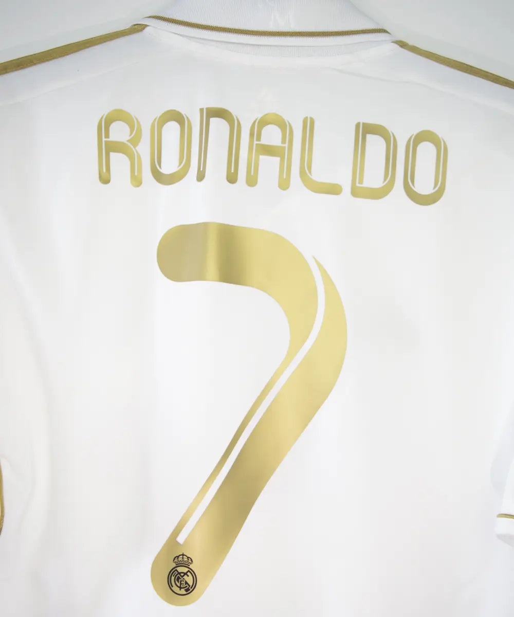 Maillot domicile du real madrid de couleur blanc et or de la saison 2011-2012. On peut retrouver l'équipementier adidas et le sponsor bwin. Le maillot est floqué du numéro 7 Cristiano Ronaldo. L'étiquette du maillot comporte les numéro V13659