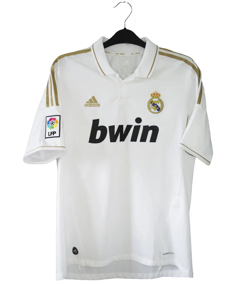 Maillot domicile du real madrid de couleur blanc et or de la saison 2011-2012. On peut retrouver l'équipementier adidas et le sponsor bwin. Le maillot est floqué du numéro 7 Cristiano Ronaldo. L'étiquette du maillot comporte les numéro V13659