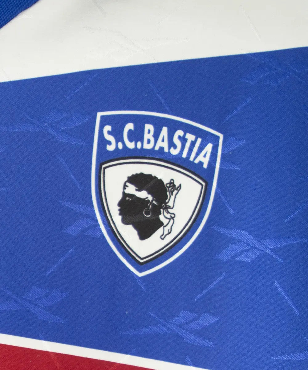 Maillot domicile bleu et blanc du sc bastia de la saison 1995-1997. On peut retrouver l'équipementier reebok, et le sponsor nouvelles frontières. Sur cette photo on peut voir le logo du SC Bastia de près