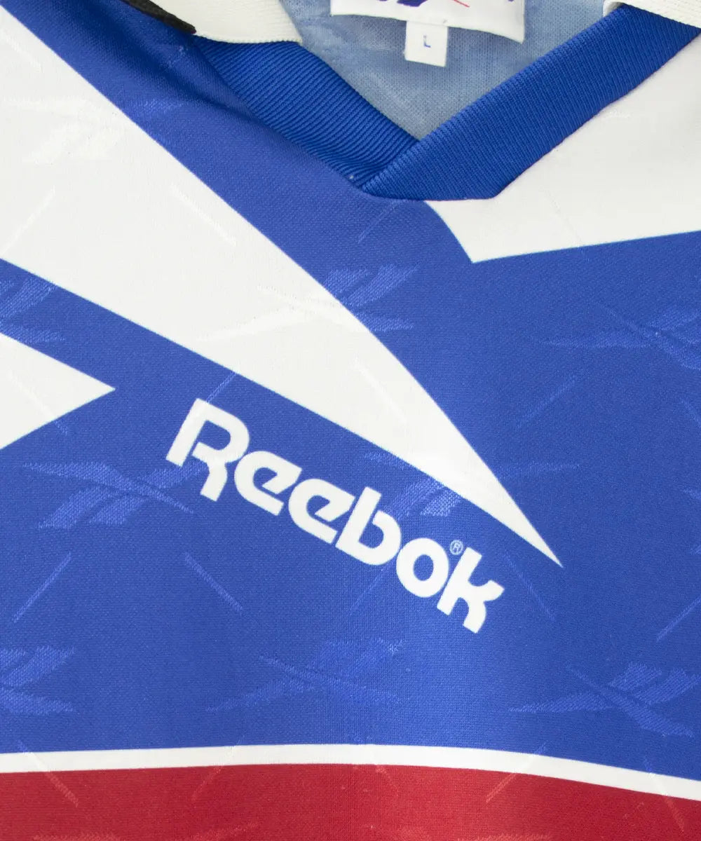 Maillot domicile bleu et blanc du sc bastia de la saison 1995-1997. On peut retrouver l'équipementier reebok, et le sponsor nouvelles frontières. Sur cette photo on peut voir le logo du Reebok de près