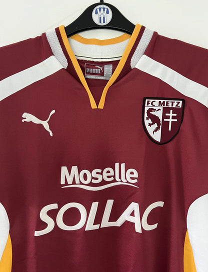 Maillot de foot vintage domicile rouge blanc et jaune du FC Metz de la saison 2001/2002. On peut retrouver l'équipementier Puma et le sponsor Sollac. Il s'agit d'un maillot authentique d'époque.