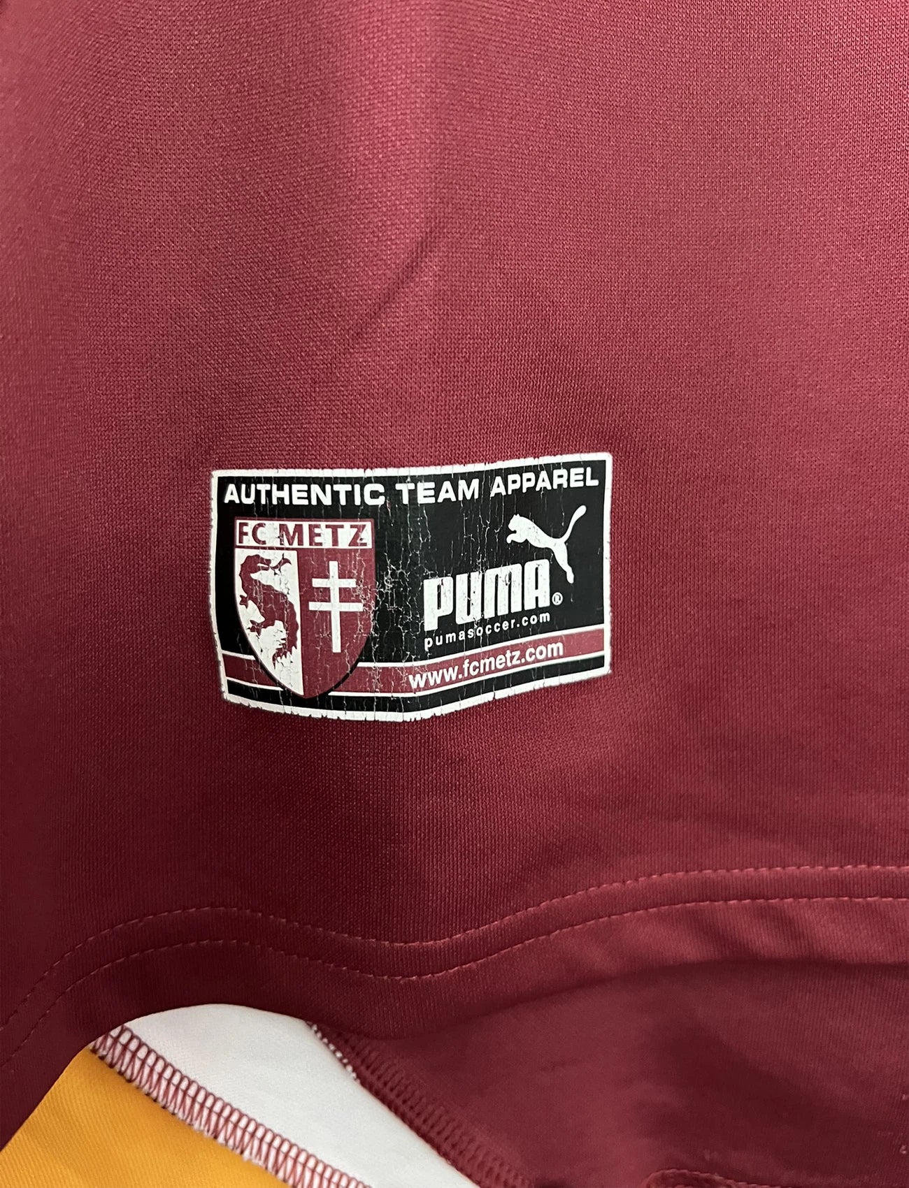 Maillot de foot vintage domicile rouge blanc et jaune du FC Metz de la saison 2001/2002. On peut retrouver l'équipementier Puma et le sponsor Sollac. Il s'agit d'un maillot authentique d'époque.