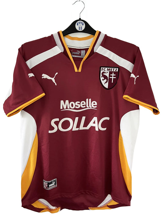 Maillot de foot vintage domicile rouge blanc et jaune du FC Metz de la saison 2001/2002. On peut retrouver l'équipementier Puma et le sponsor Sollac. Il s'agit d'un maillot authentique d'époque.