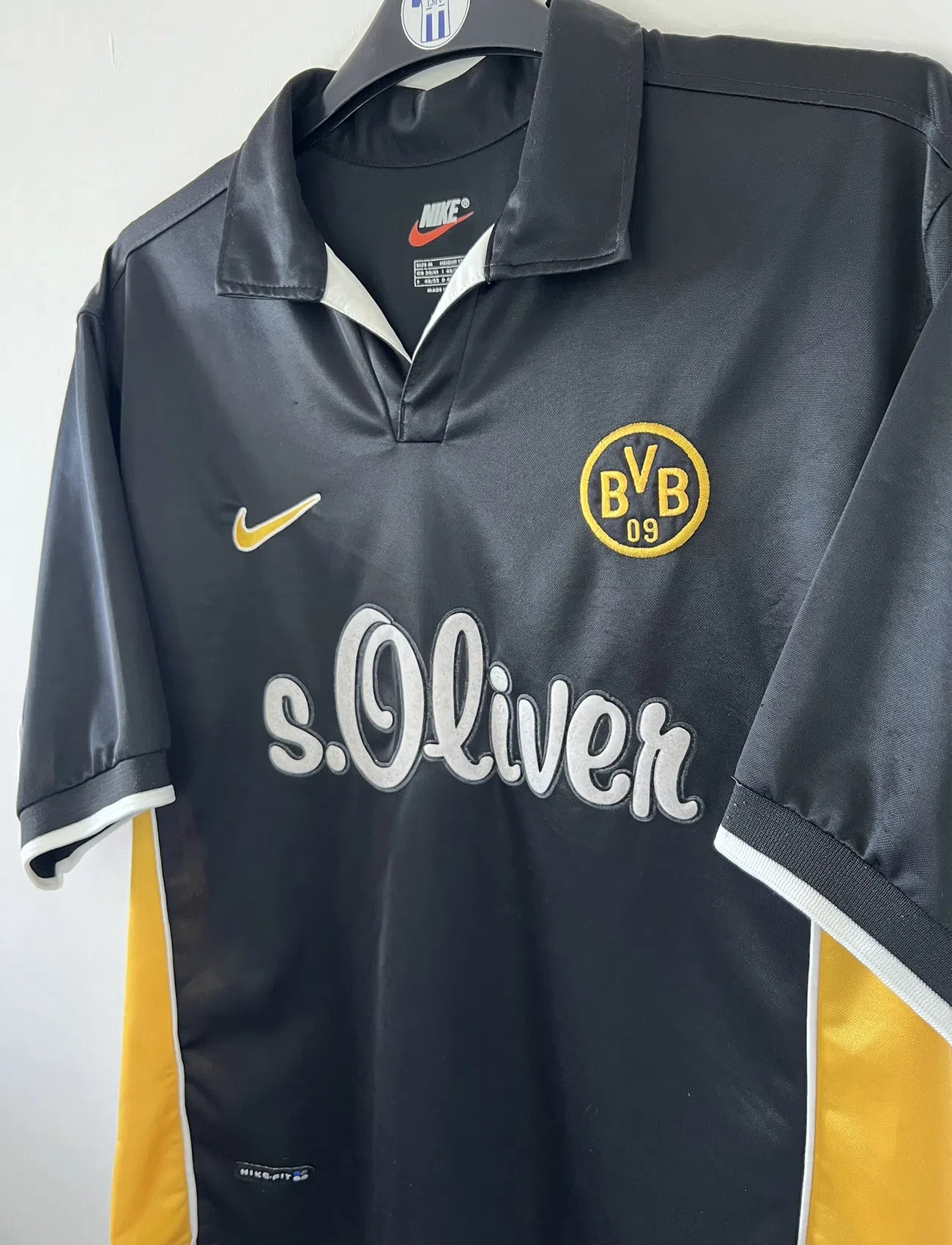 Maillot de foot vintage du Borussia Dortmund de la saison 1998/2000. Le maillot est de couleur noir et jaune. On peut retrouver l'équipementier nike et le sponsor s.Oliver. Le maillot possède l'étiquette d'authenticité F8-PKH. Il s'agit d'un maillot authentique d'époque.