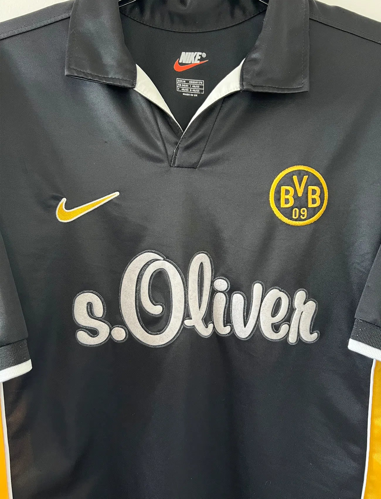 Maillot de foot vintage du Borussia Dortmund de la saison 1998/2000. Le maillot est de couleur noir et jaune. On peut retrouver l'équipementier nike et le sponsor s.Oliver. Le maillot possède l'étiquette d'authenticité F8-PKH. Il s'agit d'un maillot authentique d'époque.