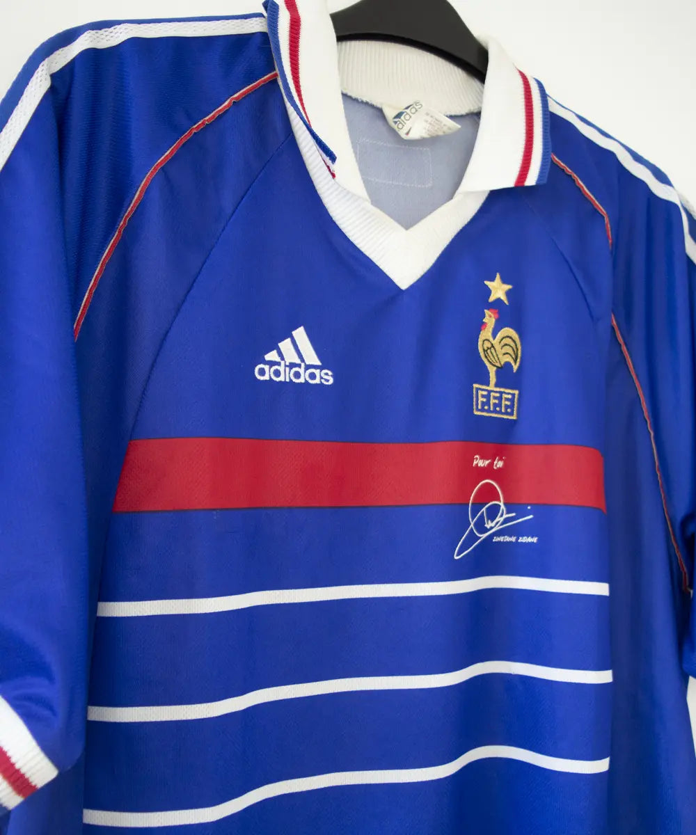 Maillot de l'équipe de france 1998 domicile de couleur bleu blanc et rouge. Le maillot est signé zinedine zidane. On peut retrouver l'équipementier adidas sur le maillot