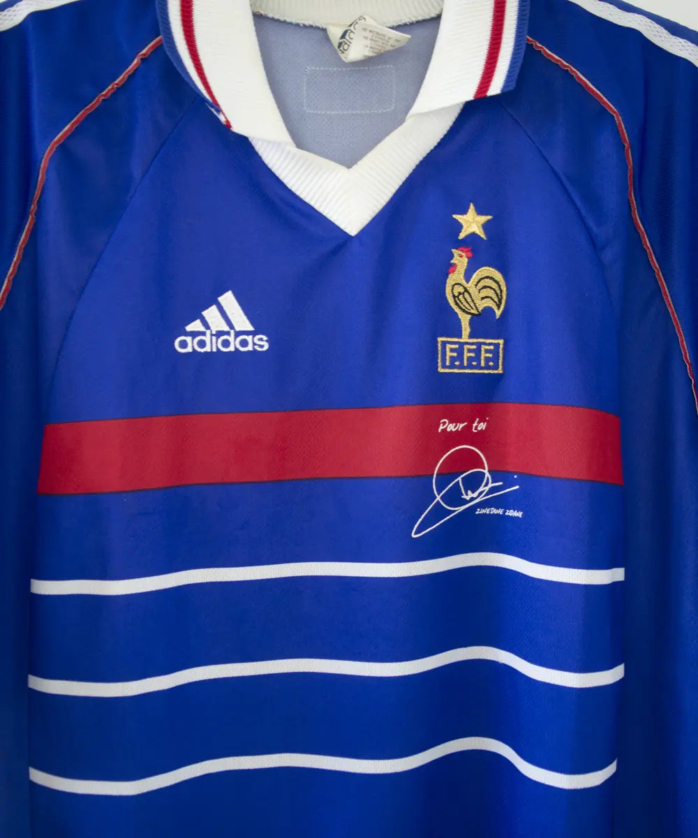 Maillot de l'équipe de france 1998 domicile de couleur bleu blanc et rouge. Le maillot est signé zinedine zidane. On peut retrouver l'équipementier adidas sur le maillot