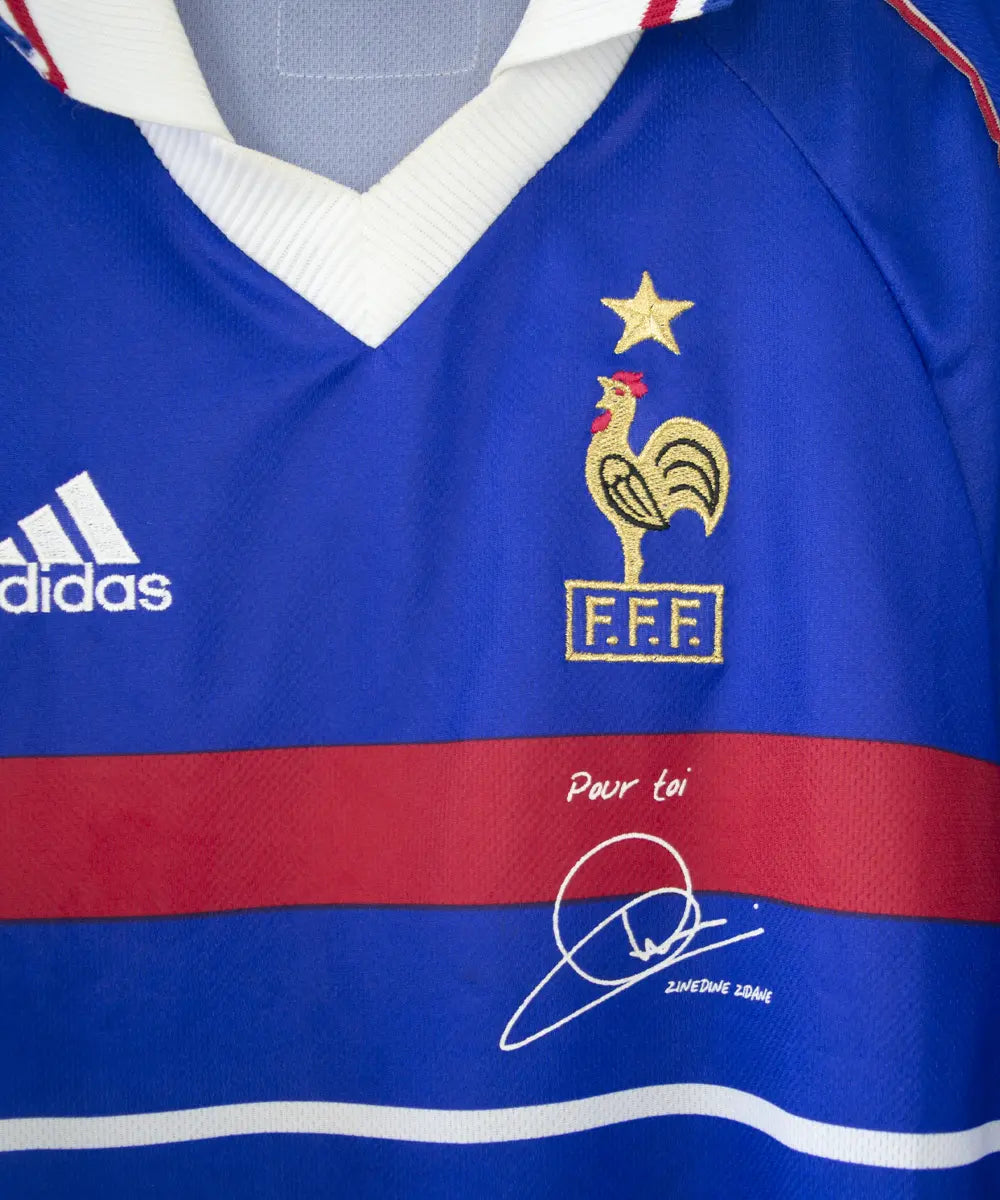 Maillot de l'équipe de france 1998 domicile de couleur bleu blanc et rouge. Le maillot est signé zinedine zidane. On peut retrouver l'équipementier adidas sur le maillot