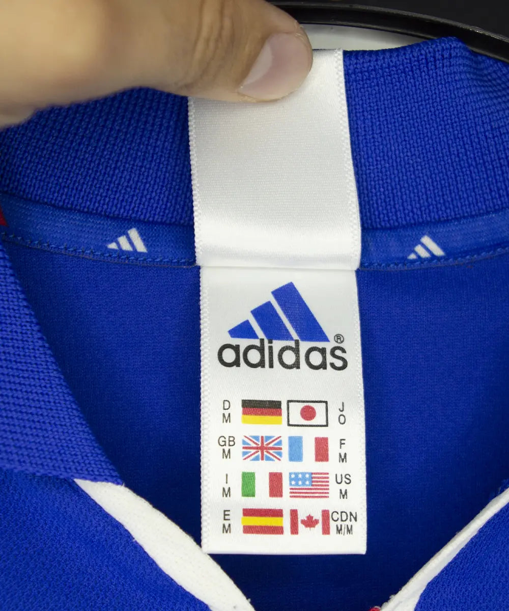 Maillot domicile bleu blanc et rouge de l'équipe de france 2000. On peut retrouver l'équipementier adidas. Sur cette photo on peut voir l'étiquette adidas