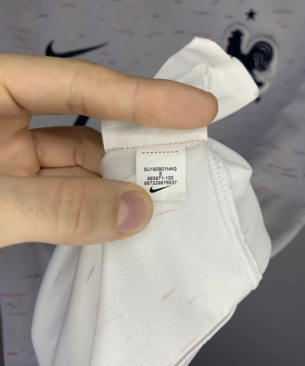 Maillot vintage extérieur blanc de l'Equipe de France 2018. On peut retrouver l'équipementier nike. Le maillot est floqué du numéro 7 Griezmann. Sur cette photo on peut voir l'étiquette d'authenticité comportant les numéros 893871-100