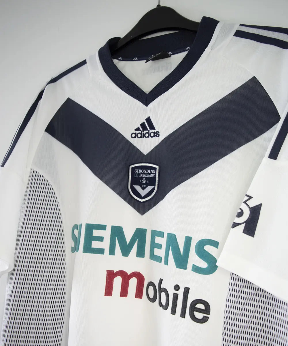 Maillot extérieur des girondins de bordeaux de couleur blanc et bleu. On peut retrouver l'équipementier adidas et le sponsor siemens mobile et M6. L'étiquette du maillot comporte les numéros AKU001