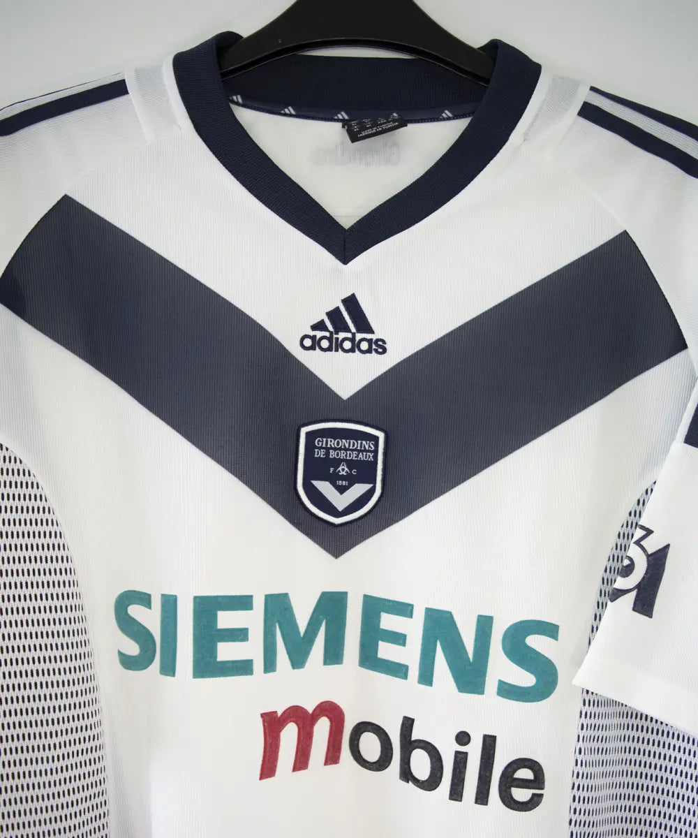 Maillot extérieur des girondins de bordeaux de couleur blanc et bleu. On peut retrouver l'équipementier adidas et le sponsor siemens mobile et M6. L'étiquette du maillot comporte les numéros AKU001