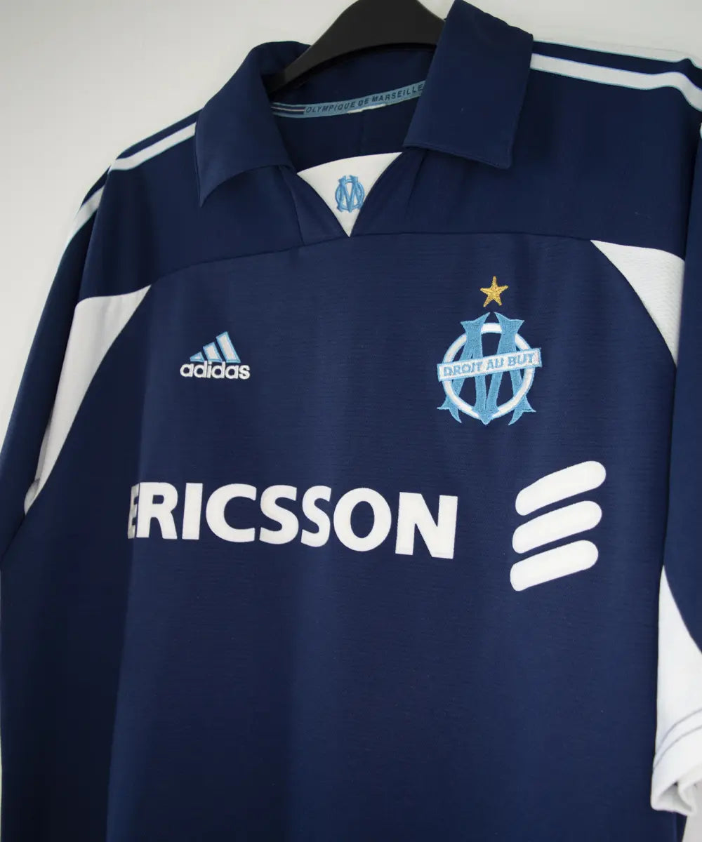 Maillot vintage extérieur bleu et blanc de l'om de la saison 1999-2000. On peut retrouver l'équipementier adidas et le sponsor ericsson