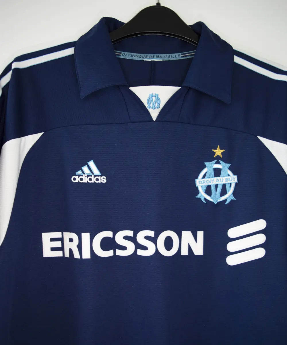 Maillot vintage extérieur bleu et blanc de l'om de la saison 1999-2000. On peut retrouver l'équipementier adidas et le sponsor ericsson
