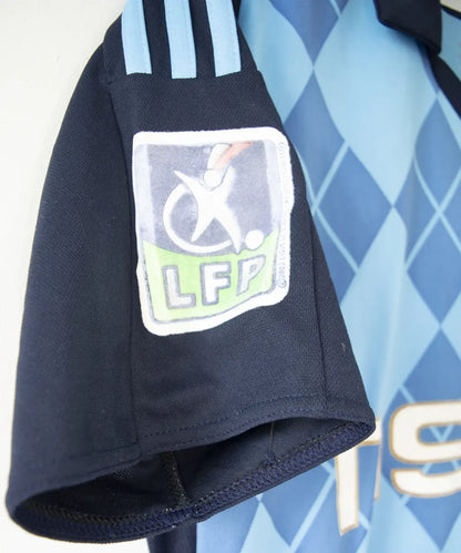 Maillot extérieur bleu clair et bleu foncé de l'om de la saison 2008-2009. Le maillot est floqué du numéro 20 Ben Arfa. On peut retrouver sur le maillot, l'équipementier adidas, le sponsor neuf, le sponsor nasuba et le sponsor groupama. Sur cette photo on peut voir le patch lfp