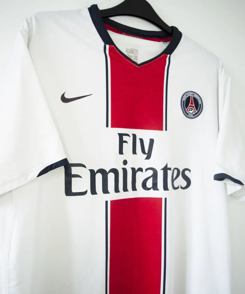 Maillot extérieur du psg de la saison 2007-2008. Le maillot est de couleur blanc, rouge et bleu. On peut retrouver l'équipementier nike et le sponsor fly emirates