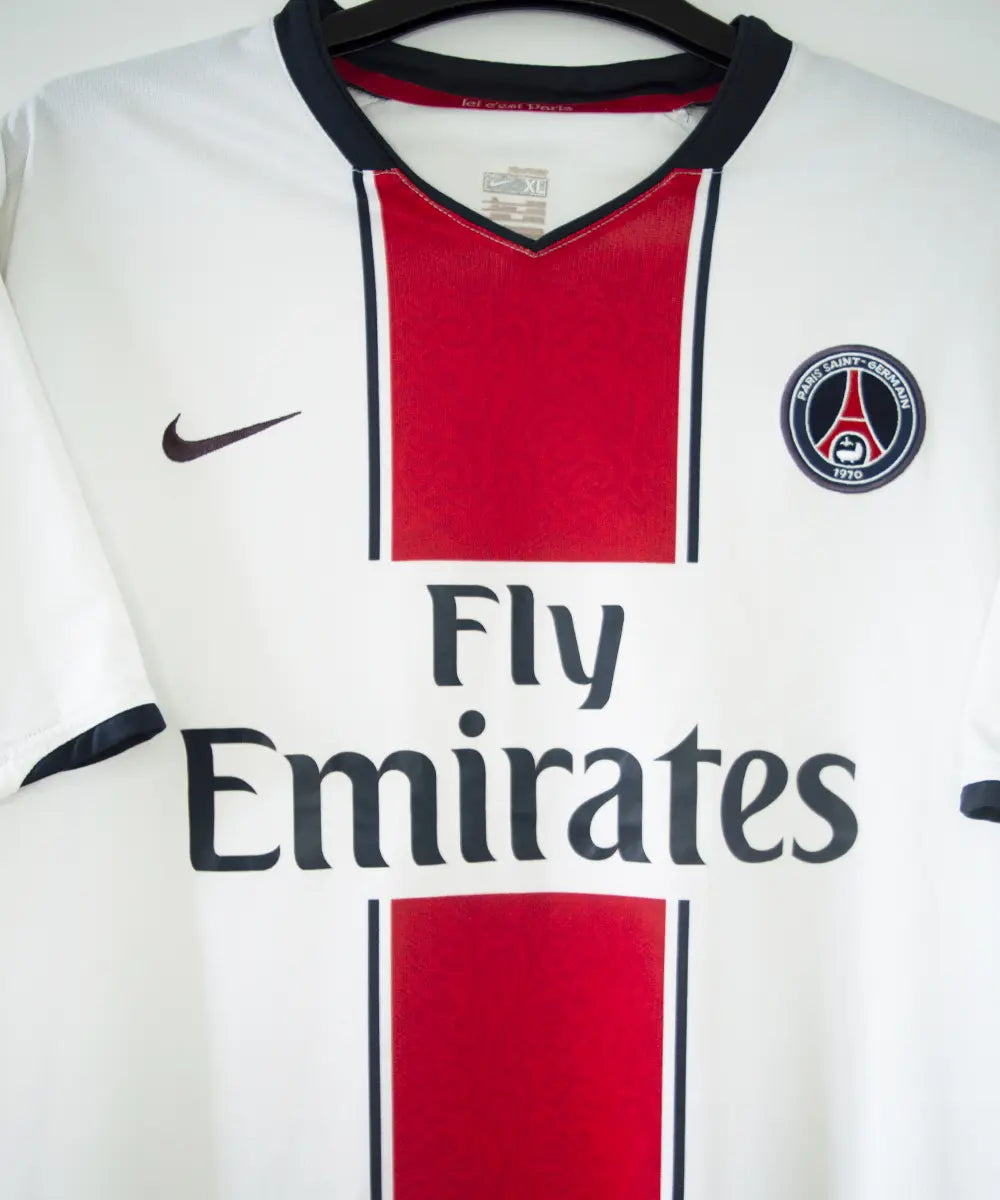 Maillot extérieur du psg de la saison 2007-2008. Le maillot est de couleur blanc, rouge et bleu. On peut retrouver l'équipementier nike et le sponsor fly emirates