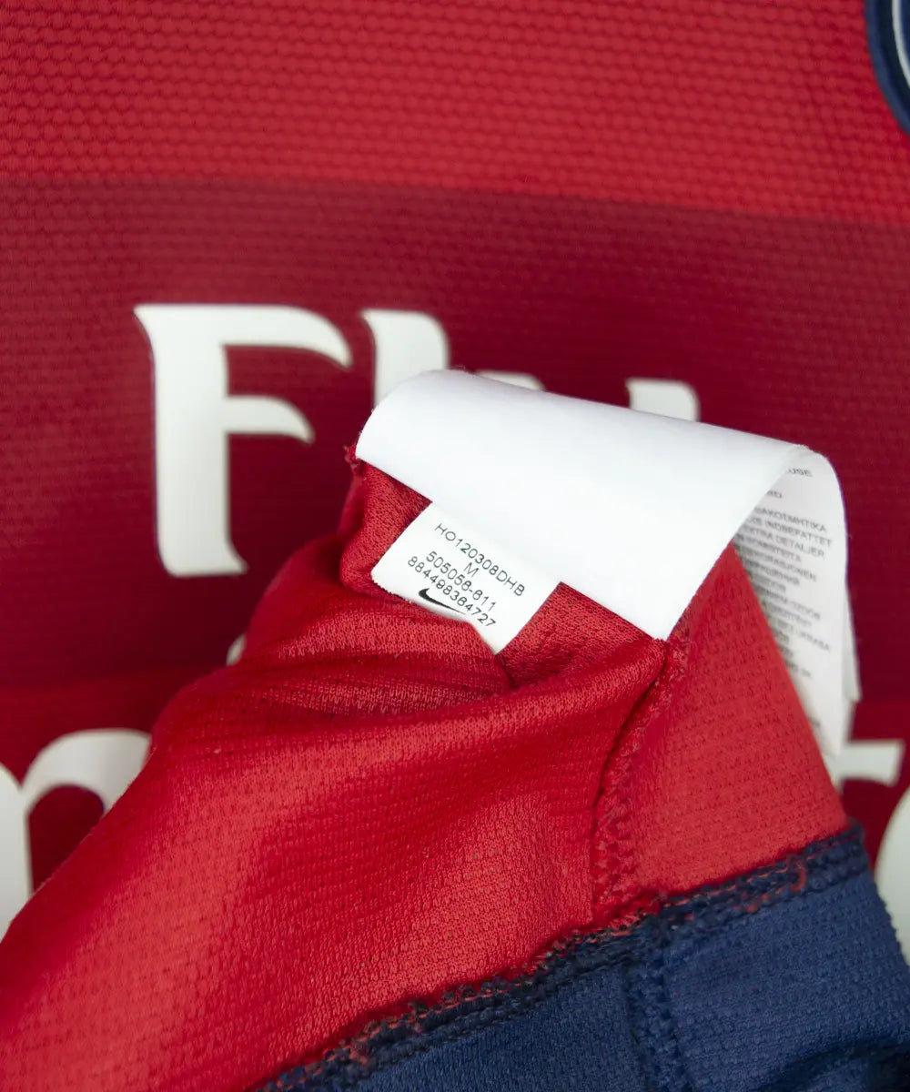 Maillot extérieur rouge du psg de la saison 2012-2013. On peut retrouver l'équipementier nike et le sponsor fly emirates. Le maillot est floqué du numéro 32 David Beckham. Sur cette photo on peut voir l'étiquette d'authenticité comportant les numéros 505056-611