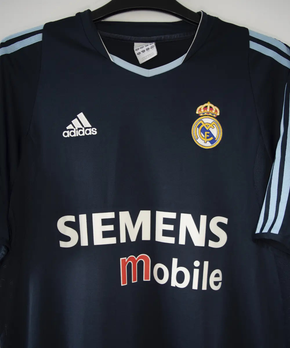 Maillot de foot vintage noir et bleu du real madrid de la saison 2003-2004. On peut retrouver l'équipementier adidas et le sponsor siemens mobile. Le maillot est floqué du numéro 23 Beckham. Il s'agit d'un maillot authentique.